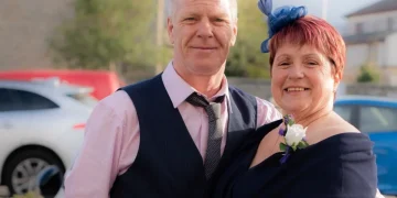 Uomo e donna posano abbracciati sorridendo, vestiti eleganti all'aperto.