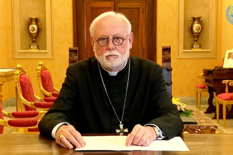 Arcivescovo Gallagher al tavolo, indossa abito clericale e occhiali.
