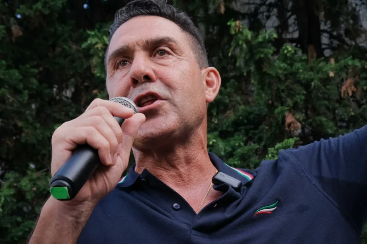 Roberto Vannacci parla al microfono con polo blu e ricami tricolore.