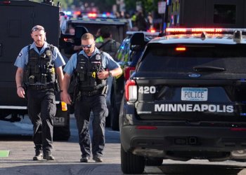Due agenti di polizia camminano vicino a un veicolo di Minneapolis.Sparatoria a Minneapolis, due morti e diversi feriti in un condominio: ucciso il killer