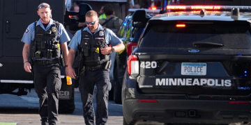 Due agenti di polizia camminano vicino a un veicolo di Minneapolis.Sparatoria a Minneapolis, due morti e diversi feriti in un condominio: ucciso il killer