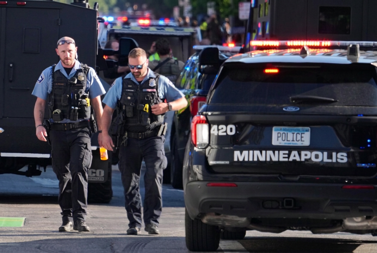 Due agenti di polizia camminano vicino a un veicolo di Minneapolis.Sparatoria a Minneapolis, due morti e diversi feriti in un condominio: ucciso il killer