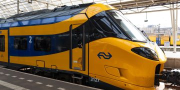A modern yellow and blue train at an Amsterdam station platform under a glass roof. Paesi Bassi, sabotaggio ai treni: circolazione bloccata in gran parte del Paese