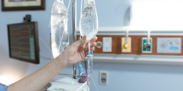 Close-up image of an IV drip and hand in a hospital room, illustrating medical care.