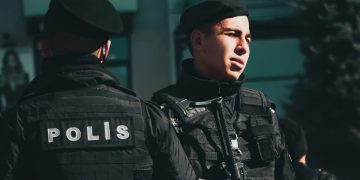 Two police officers in tactical gear standing with rifles during the day. Turchia, spari fuori scuola: 8 studenti feriti, arrestato l'aggressore
