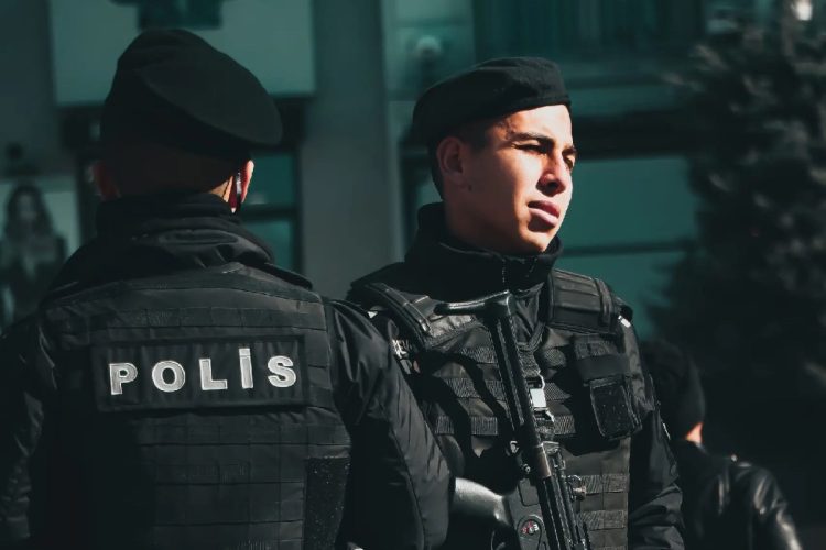 Two police officers in tactical gear standing with rifles during the day. Turchia, spari fuori scuola: 8 studenti feriti, arrestato l'aggressore