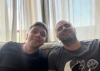 Due uomini sorridenti seduti sul divano in casa, atmosfera serena. Di Battista: "Sto molto meglio, finalmente sono a casa"