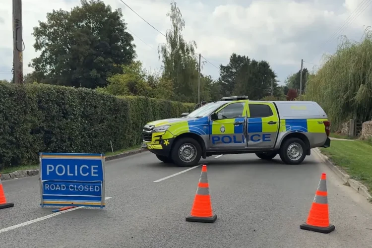 Furgone della polizia britannica blocca una strada rurale con segnali.