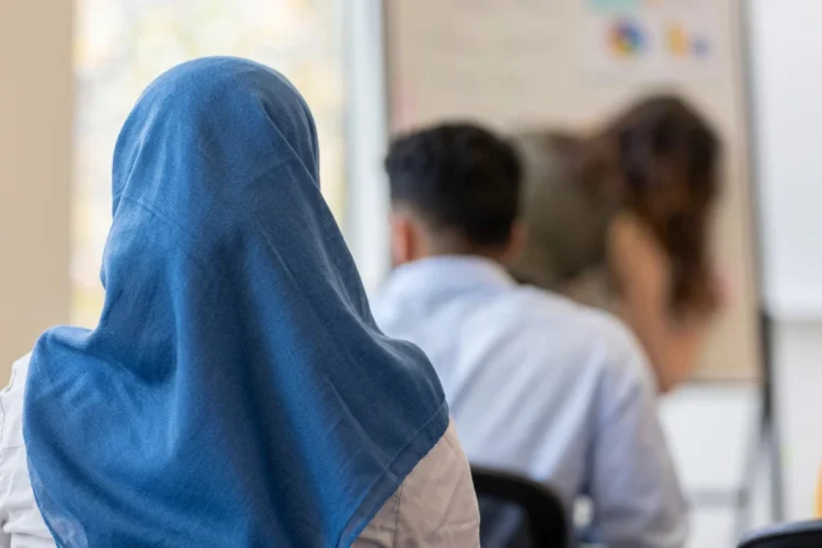 Ragazza con velo islamico siede tra studenti in un’aula.