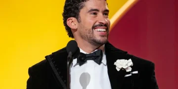 Uomo sorridente con smoking nero tiene in mano un premio Grammy
