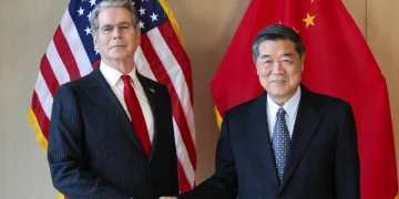 Due politici si stringono la mano davanti alle bandiere di USA e Cina.