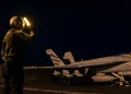Membro personale di terra dirige F-18 Hornet su portaerei di notte.