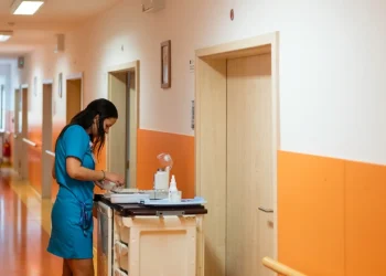 Infermiere in camice blu prepara farmaci su carrello ospedaliero corridoio.
