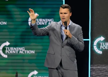 Charlie Kirk parla al microfono in completo grigio su un palco.