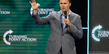 Charlie Kirk parla al microfono in completo grigio su un palco.