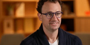 Dario Amodei, CEO di Anthropic, indossa occhiali e cardigan blu.