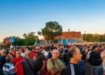 Folla di operai e manifestanti radunati presso un complesso industriale.
