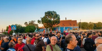Folla di operai e manifestanti radunati presso un complesso industriale.