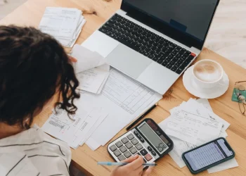 Giovane calcola tasse e fatture su scrivania con computer e telefono.