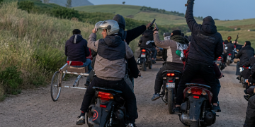 Uomini su moto in campagna, alcuni sollevano fucili e pistole. Catania, kalashnikov alla corsa clandestina di cavalli: arrestato un giovane