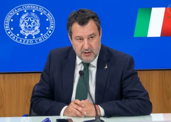 Matteo Salvini parla al microfono con sfondo Palazzo Chigi e bandiera italiana.