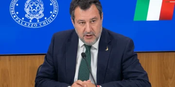 Matteo Salvini parla al microfono con sfondo Palazzo Chigi e bandiera italiana.