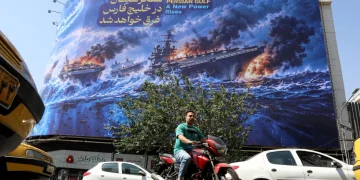 Iranians drive next to an anti-US billboard