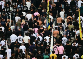 Tifosi della Juventus di spalle in curva allo stadio, alcuni con maglie storiche.