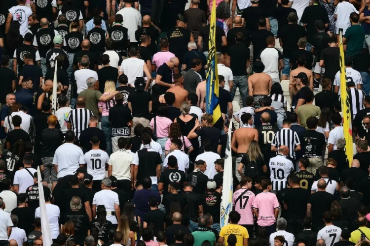 Tifosi della Juventus di spalle in curva allo stadio, alcuni con maglie storiche.