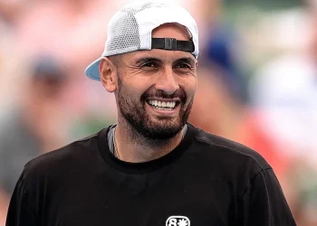Tennista Nick Kyrgios sorride in campo con un cappellino bianco.