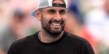 Tennista Nick Kyrgios sorride in campo con un cappellino bianco.