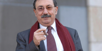 Fabio Mussi sorride con occhiali e sigaro, sciarpa bordeaux. È morto Fabio Mussi, ex ministro e storico esponente della sinistra