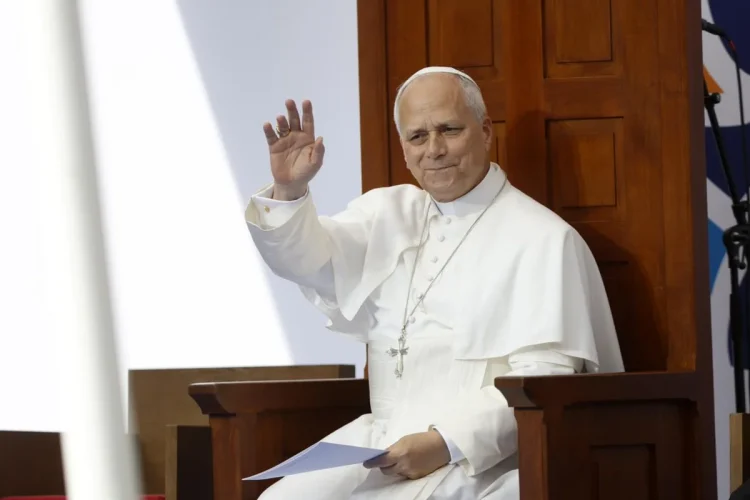Papa Leone XIV saluta il pubblico, vestito di bianco, seduto.