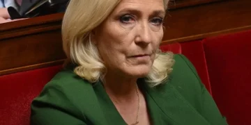 Marine Le Pen guarda in camera, giacca verde, seduta in parlamento.