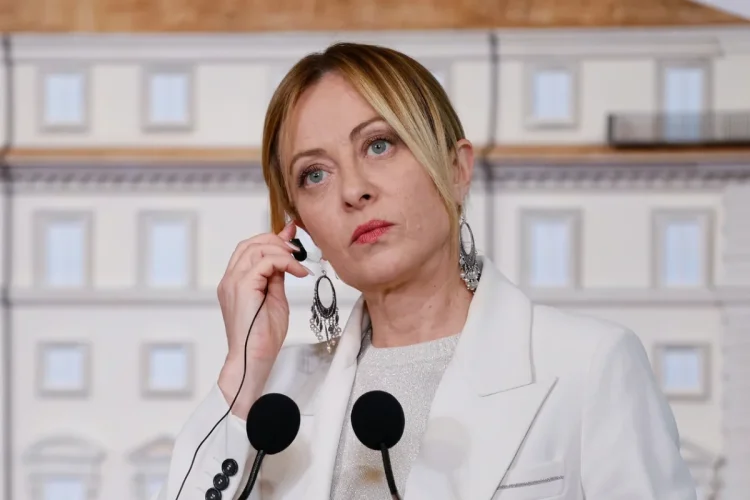 Giorgia Meloni, espressione seria, con auricolare e microfoni durante un discorso.