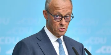 Friedrich Merz parla con espressione seria davanti ai microfoni.