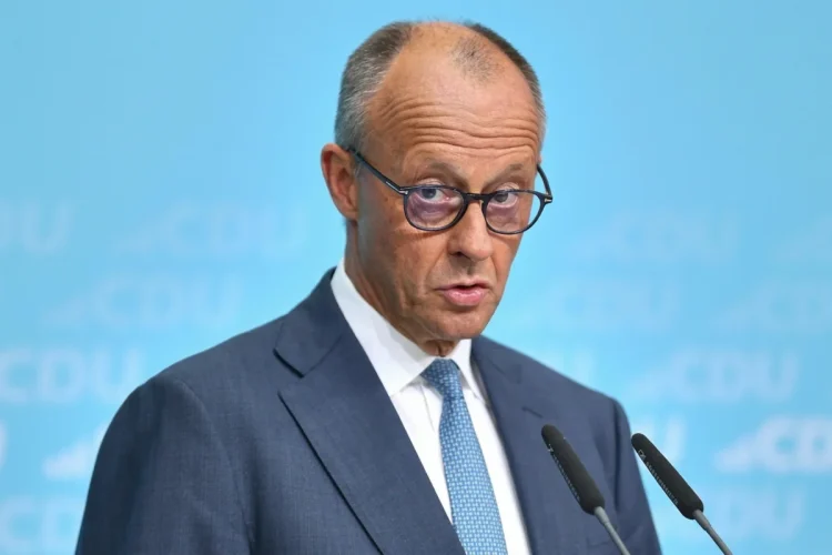 Friedrich Merz parla con espressione seria davanti ai microfoni.
