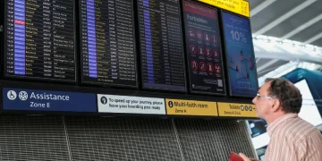 Uomo guarda tabellone voli cancellati in aeroporto britannico