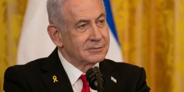 Benjamin Netanyahu indossa spilla gialla e cravatta rossa al microfono.