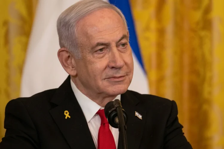 Benjamin Netanyahu indossa spilla gialla e cravatta rossa al microfono.