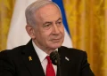Benjamin Netanyahu indossa spilla gialla e cravatta rossa al microfono.