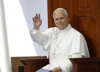 Papa Leone XIV saluta il pubblico, vestito di bianco, seduto.