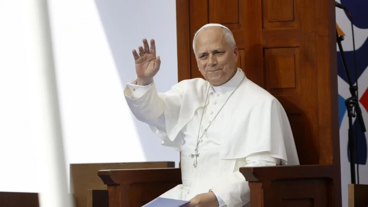 Papa Leone XIV saluta il pubblico, vestito di bianco, seduto.