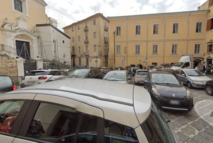 Strada trafficata con auto parcheggiate in Largo Tommaso D'Aquino, Salerno. Accoltellata alle spalle da uno sconosciuto, grave una 20enne