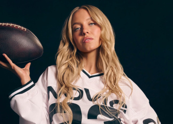Sydney Sweeney bionda in maglia sportiva con pallone da football. Atlete contro lo spot senza veli di Sydney Sweeney: "Un passo indietro per le donne"