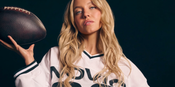 Sydney Sweeney bionda in maglia sportiva con pallone da football. Atlete contro lo spot senza veli di Sydney Sweeney: "Un passo indietro per le donne"