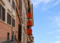 Insegna verticale rossa "BAR" su edificio romano antico, cielo azzurro