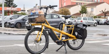 A yellow cargo e-bike carrying groceries parked outside a supermarket in France. Sanzioni fino a 15mila euro sulle e-bike: i Comuni italiani si dotano di bicivelox