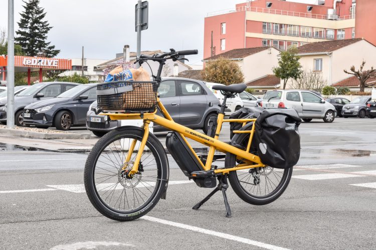 A yellow cargo e-bike carrying groceries parked outside a supermarket in France. Sanzioni fino a 15mila euro sulle e-bike: i Comuni italiani si dotano di bicivelox