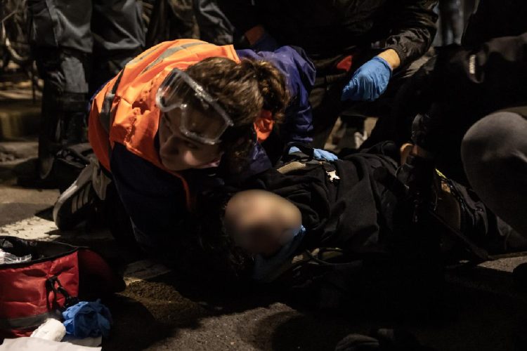 Primo piano del manifestante a terra a Bologna con un'operatrice che gli tiene la testa